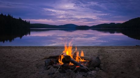 Un feu de camp qui brûle sur la plage au crépuscule, lors d'une sortie en kayak avec nuitée.